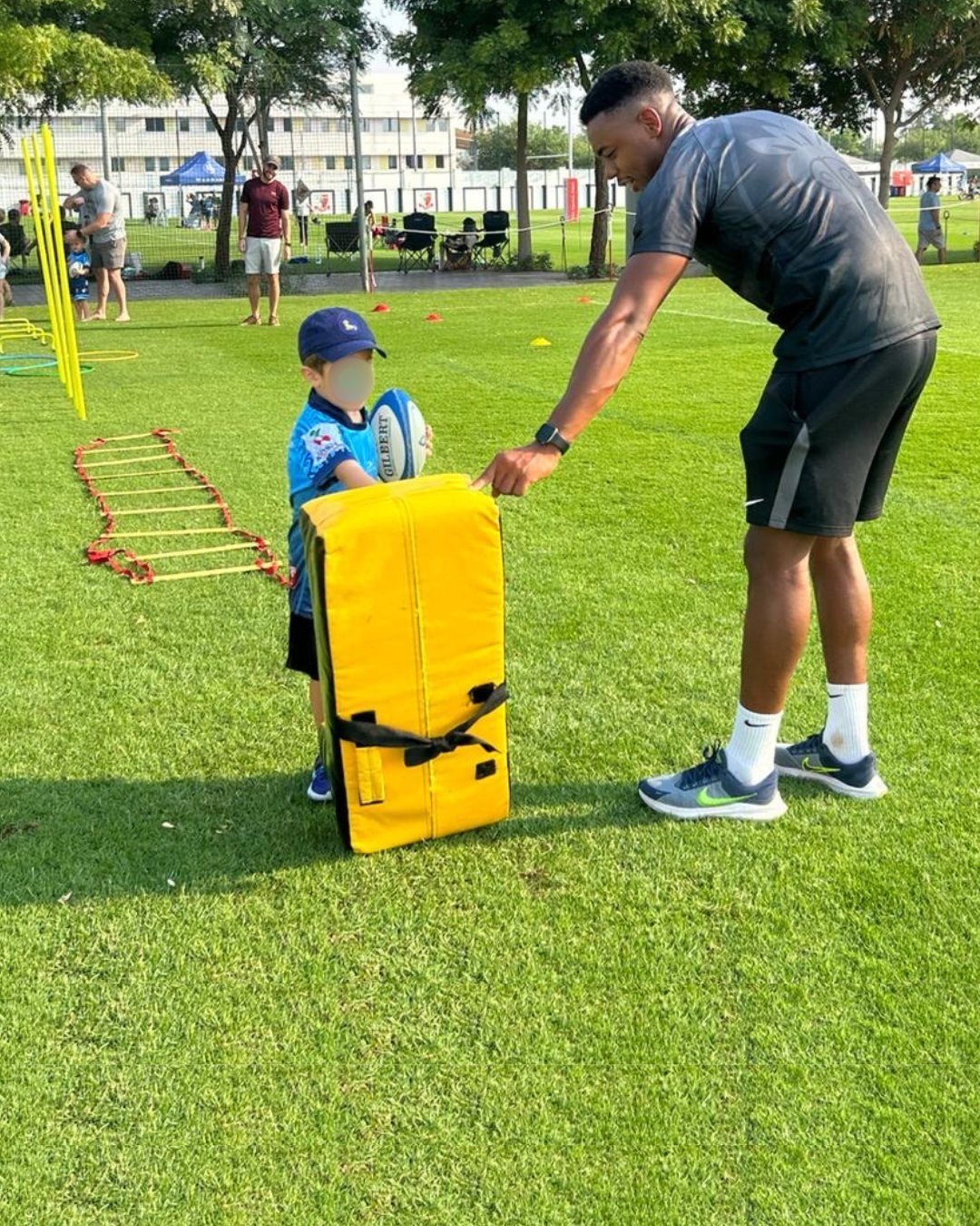 A UAE rugby coach working one to one with a young player on tackle pad technique during a session